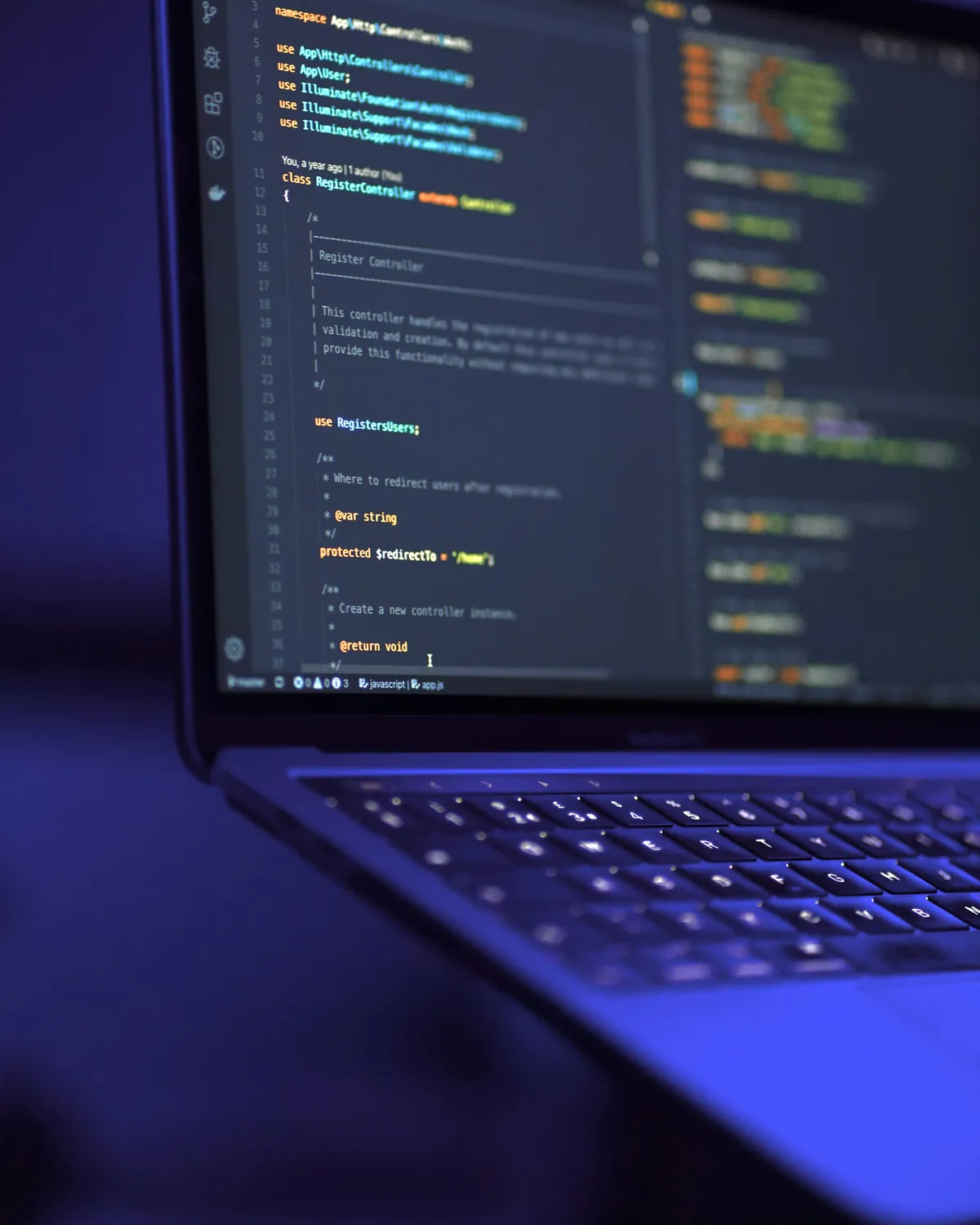 Open laptop showing code in a dark editor, keyboard lit by violet light